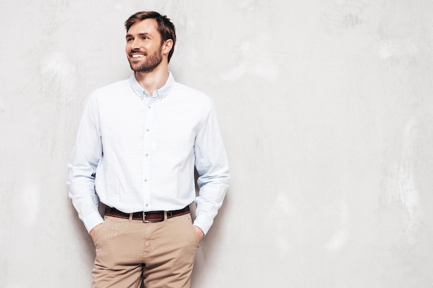 Free Photo portrait of handsome smiling model sexy stylish man dressed in shirt and trousers fashion hipster male posing near grey wall in studio isolated