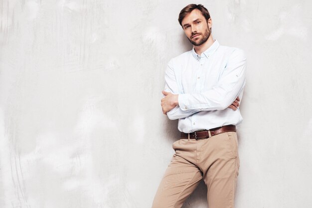 Portrait of handsome smiling model Sexy stylish man dressed in shirt and trousers Fashion hipster male posing near grey wall in studio Isolated