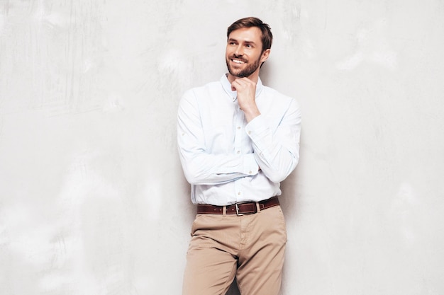 Portrait of handsome smiling model Sexy stylish man dressed in shirt and trousers Fashion hipster male posing near grey wall in studio Isolated