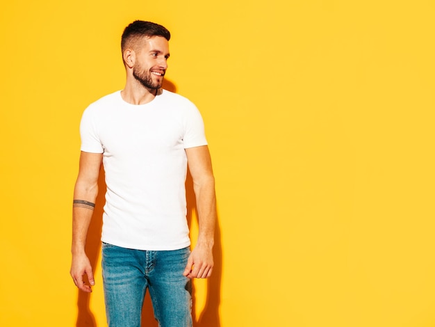 Portrait of handsome smiling model Sexy stylish man dressed in summer clothes Fashion hipster male posing near yellow wall in studio