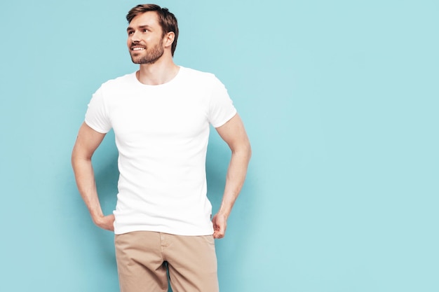 Portrait of handsome smiling stylish hipster lambersexual model Sexy man dressed in Tshirt and trousers Fashion male isolated on blue wall in studio