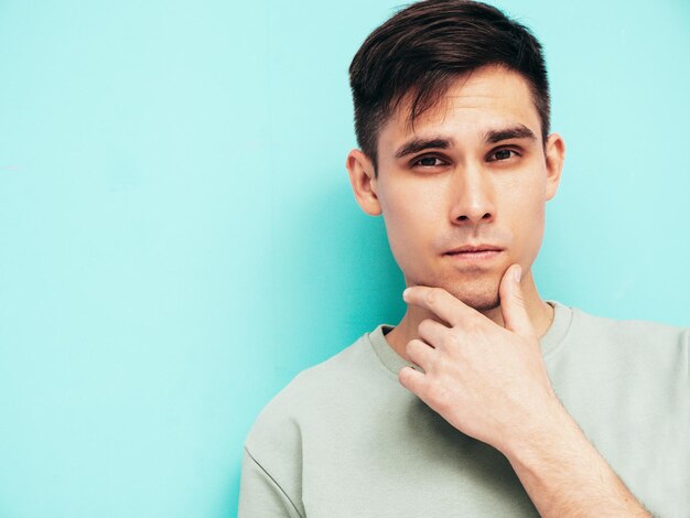 Portrait of handsome smiling stylish hipster lambersexual modelMan dressed in Tshirt and jeans Fashion male isolated in studio Posing near blue wall Cheerful and happy