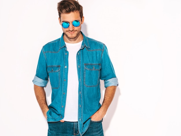 Portrait of handsome smiling stylish young man model wearing jeans clothes and sunglasses. Fashion man 