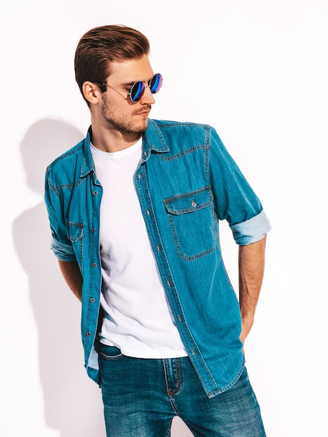 Portrait of handsome smiling stylish young man model wearing jeans clothes and sunglasses. Fashion man 