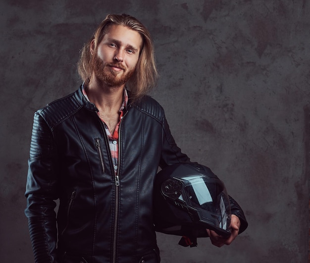 Free Photo portrait of a handsome stylish redhead biker in a black leather jacket, holds motorcycle helmet, posing in a studio. isolated on a dark background.