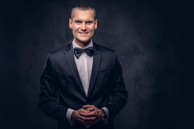 Portrait of a handsome stylish smiling male in an elegant black suit over a dark background.