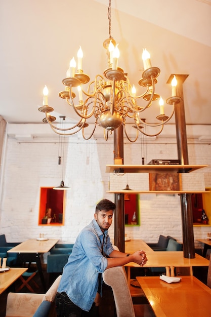 Free photo portrait of handsome successful bearded south asian young indian freelancer in blue jeans shirt standing in cafe