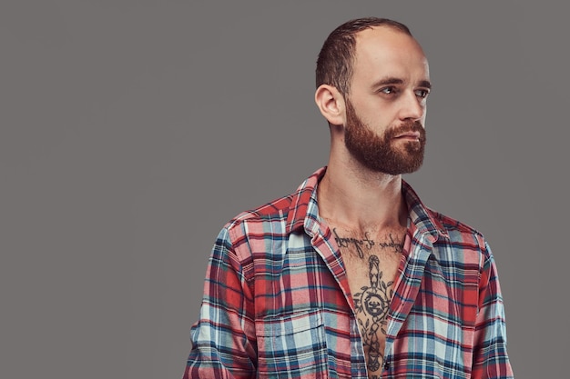 Free photo portrait of a handsome tattooed stylish hipster with a well-trimmed beard in a flannel shirt, posing in a studio. isolated on a gray.