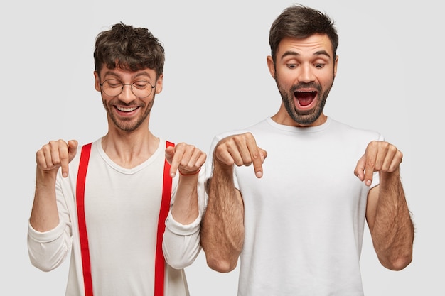 Portrait of handsome two cheerful male friends have beards, happy expressions, indicate down on floor