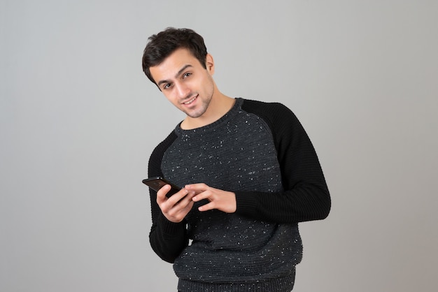 Portrait of handsome young male posing with cellphone over gray wall