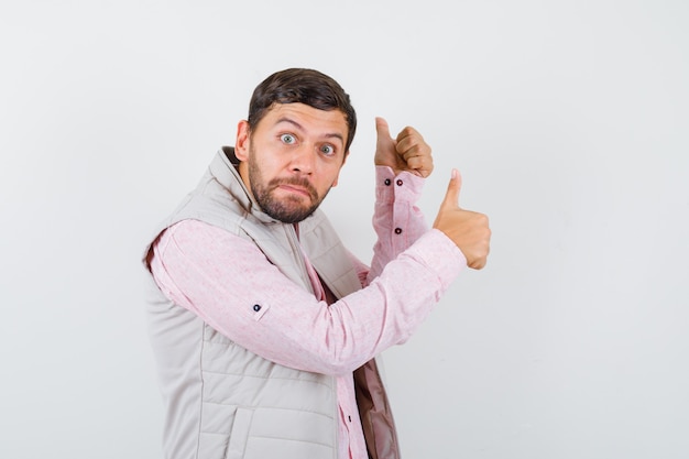 Portrait of handsome young male showing double thumbs up in shirt, vest and looking amazed front view