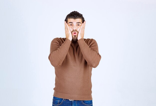 Portrait of a handsome young man in casual sweater holding palms near cheeks .