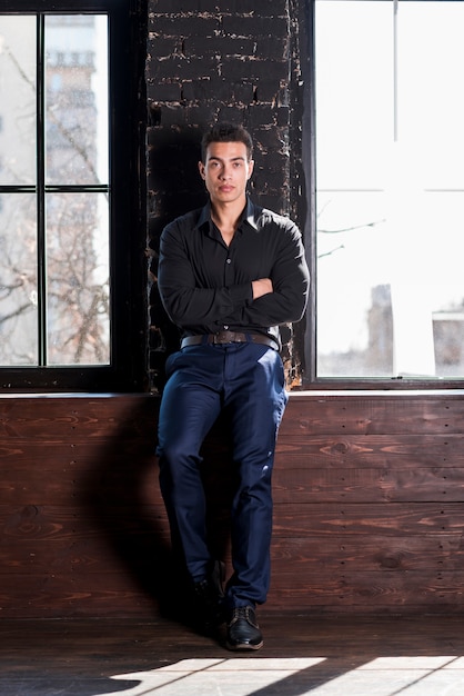 Portrait of a handsome young man leaning on wall with his arms crossed