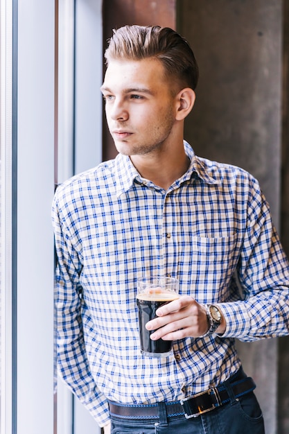 Portrait of a handsome young man leaning at window holding the beer glass