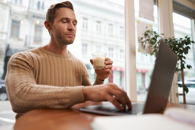 Portrait of handsome young man sitting in cafe with laptop digital nomad freelancer working outdoors