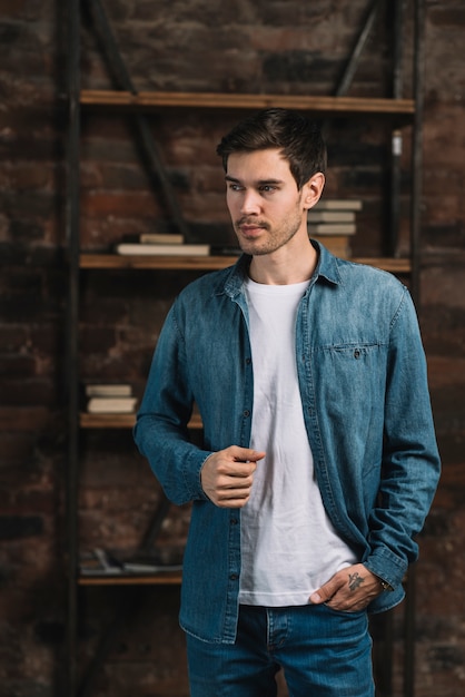 Free photo portrait of handsome young man standing in from of bookshelf