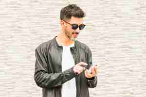 Free photo portrait of handsome young man wearing sunglasses using smartphone