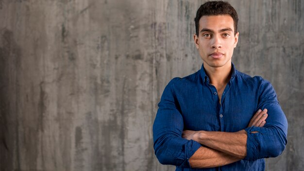 Portrait of a handsome young man with crossed arms against concrete backdrop