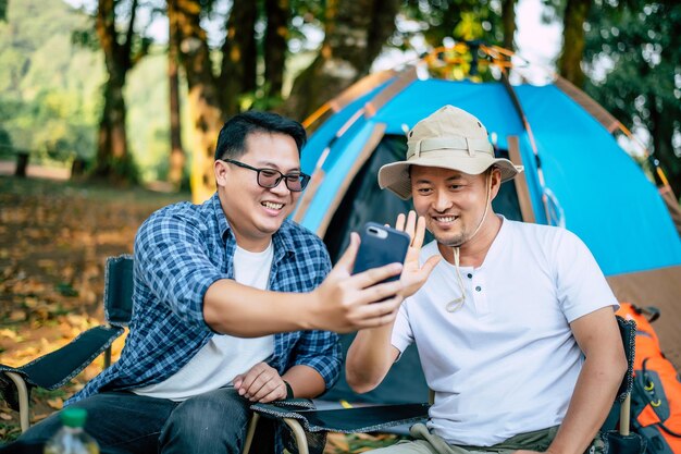 Portrait happy Asian man friends Making a video call with smartphone in camping Cooking set front ground Outdoor cooking traveling camping lifestyle concept