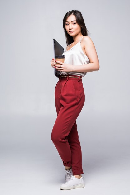 Portrait of a happy asian woman working on laptop computer isolated over white wall