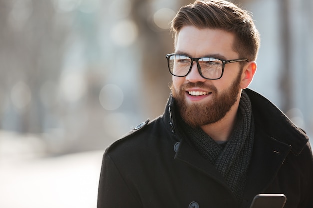 Free photo portrait of happy bearded young man in glasses standing outdoors