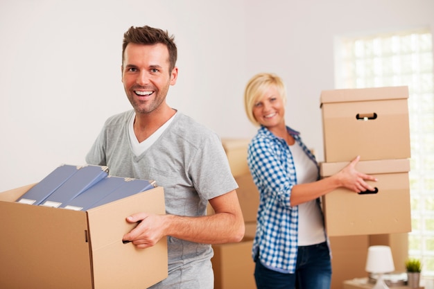 Portrait of happy couple carrying cardboard boxes in new home