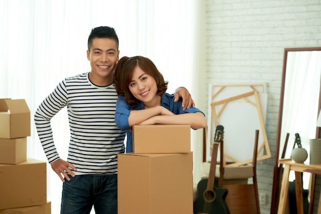 Portrait of happy couple posing at package boxes before relocation to the new apartment