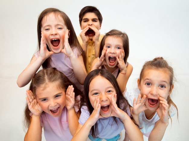 The portrait of happy cute little kids boy and girls in stylish casual clothes looking at front against white studio wall