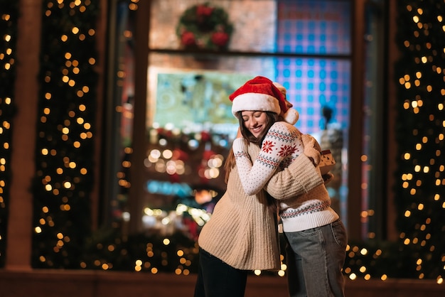 Portrait of happy cute young friends hugging each other and smiling while walking at christmas eve outdoors.