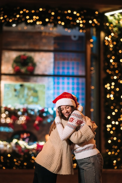 Free photo portrait of happy cute young friends hugging each other and smiling while walking at christmas eve outdoors.