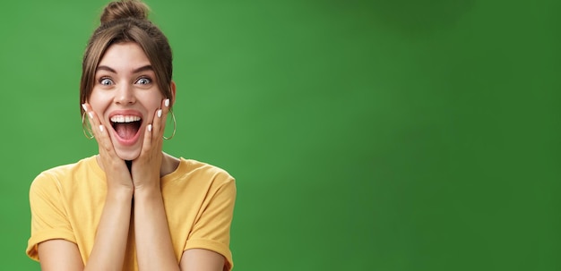 Free Photo portrait of happy delighted and surprised young feminine girl in yellow tshirt pressing hands to