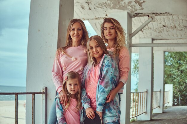 Portrait of a happy family dressed in stylish clothes holds skateboards posing near a guardrail against a sea coast.