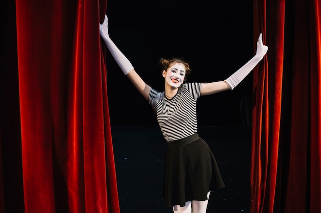 Free photo portrait of a happy female mime artist holding red curtain