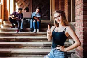 Free photo portrait of a happy female student stay near campus with okay sign. success and education concept.