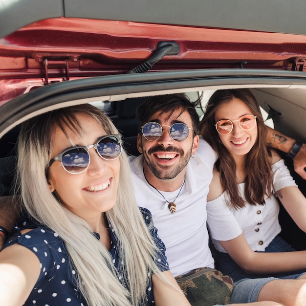 Portrait of happy friends sitting inside the car trunk