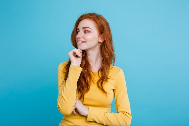 Portrait of happy ginger red hair girl with freckles smiling looking at camera. Pastel blue background. Copy Space.