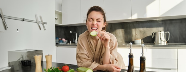 Free photo portrait of happy girl eating vegetables while making meal cooking healthy vegetarian food in