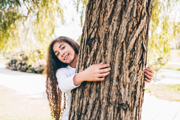 Portrait of a happy girl hugging large trunk in the garden