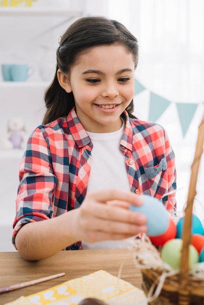 Portrait of a happy girl removing blue easter egg from the basket on table