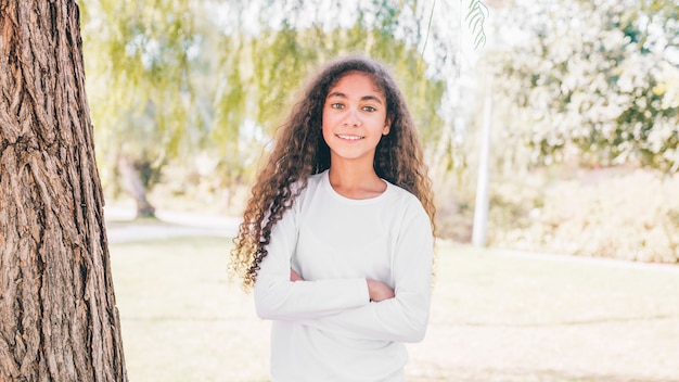 Free Photo portrait of a happy girl with arm crossed standing in the garden