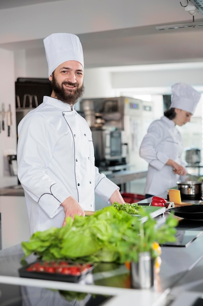 Free photo portrait of happy head chef wearing cooking uniform, standing in restaurant professional kitchen while smiling at camera. gourmet cuisine skilled expert preparing recipe ingredients for meal dish.