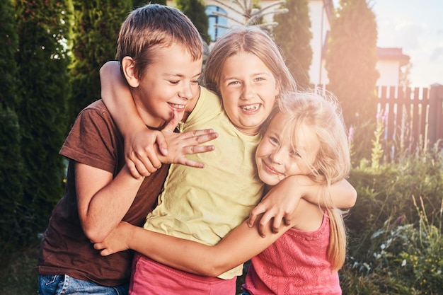 Portrait of happy little friends having fun at yard. Three cute little friends cuddling and play.