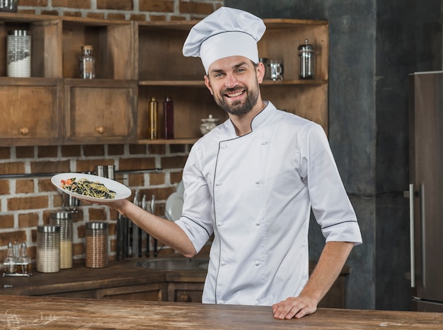 Free photo portrait of happy male chef presenting tasty spaghetti dish