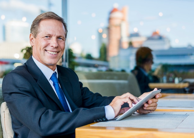 Free photo portrait of a happy mature businessman using digital tablet in restaurant