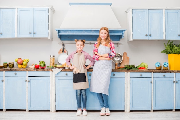 Portrait of happy mother and daughter in apron standing in the kitchen