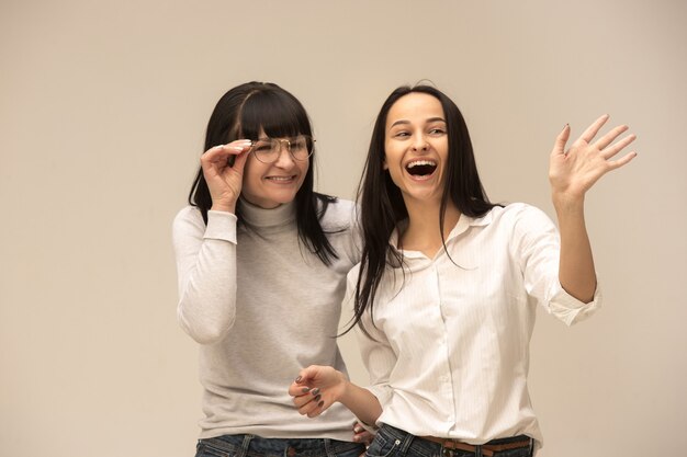 A portrait of a happy mother and daughter at studio on gray background. Human positive emotions and facial expressions concept