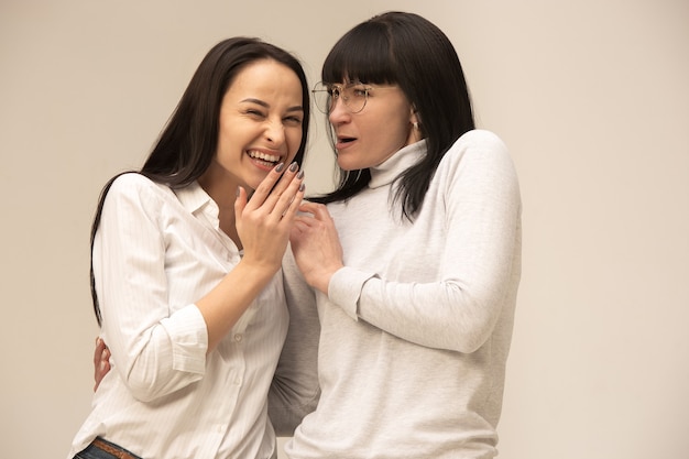 A portrait of a happy mother and daughter at studio on gray background. Human positive emotions and facial expressions concept