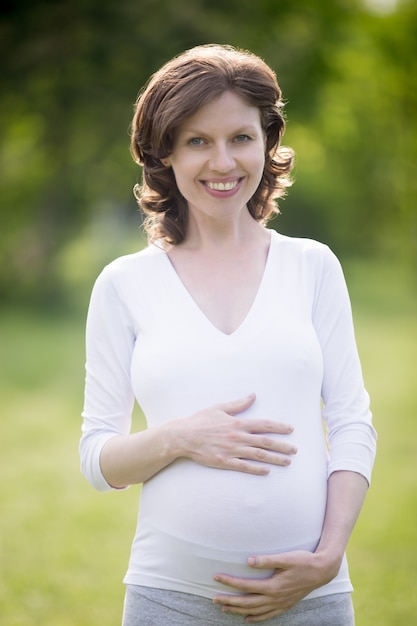 Portrait of happy pregnant female touching her belly