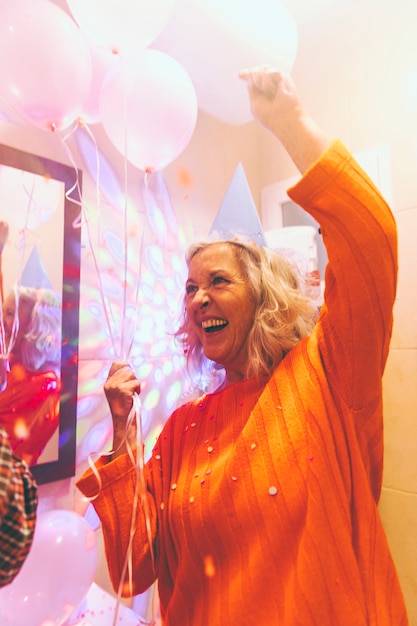 Portrait of a happy senior woman holding balloons in hand enjoying at birthday party