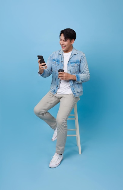 Portrait happy smiling young asian man using smartphone sitting on chair